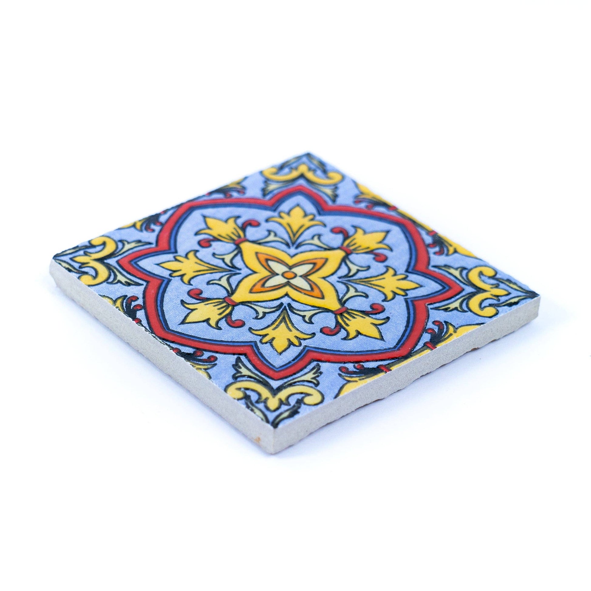 The Tile-Inspired Ceramic & Cork Coasters - Set of 6 by Meninas Bonitas Cork features vibrant blue, yellow, red, and black floral and geometric patterns on light blue—shown at an angle on a white surface. Perfect as Portuguese-style coasters.