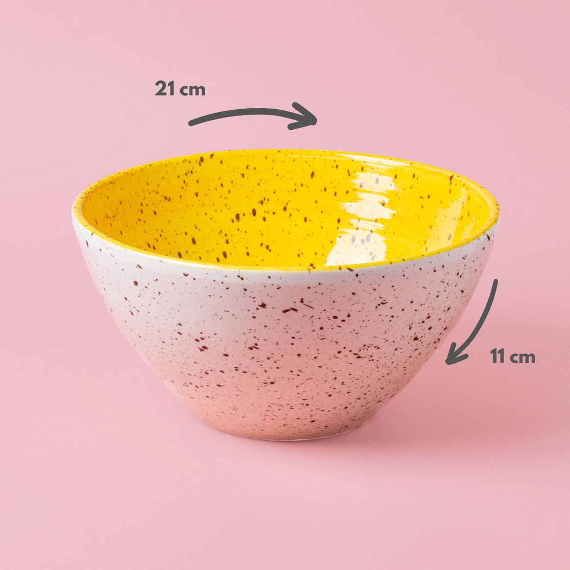The CANELA Oil and Salad Bowl by Alfar Tierra Cocida is a speckled ceramic piece with a yellow glazed interior, measuring 21 cm wide and 11 cm tall, displayed on a pink background.