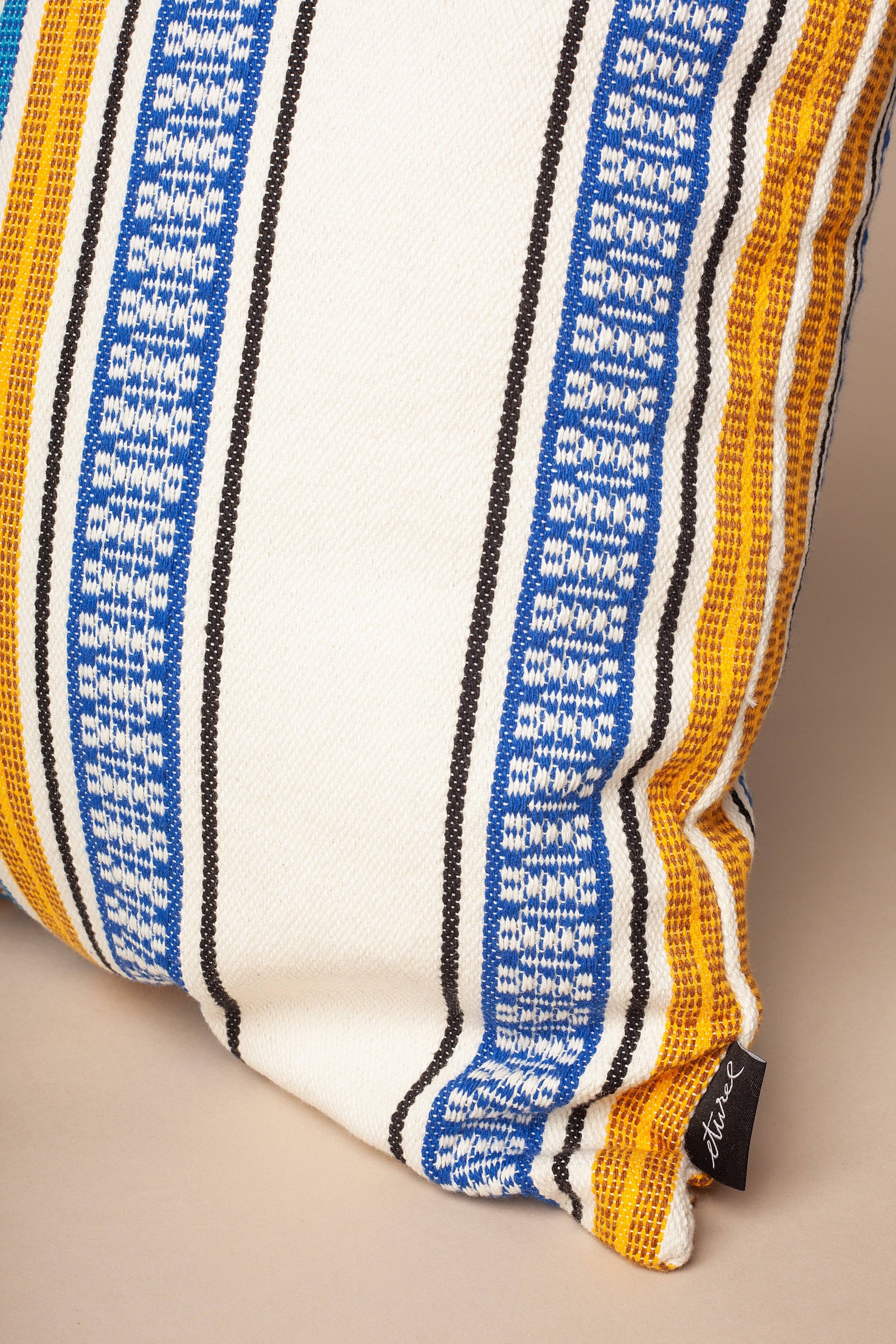 A close-up of the Eturel Madrid Morellano Blue Woven Cushion Cover 50cmx50cm, featuring vertical blue, yellow, black, and white stripes and a small black tag with white text on the side.