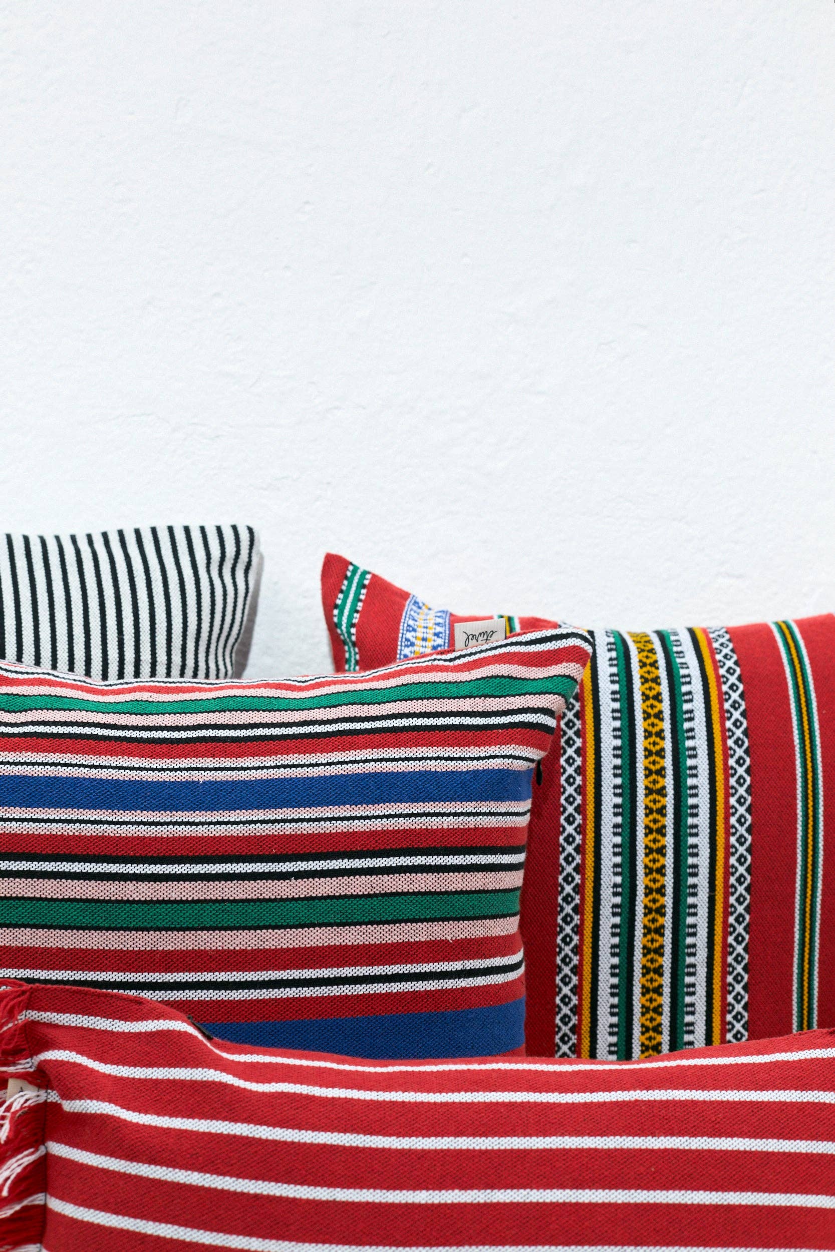 Four vibrant Red Pomegranate Cushion Covers (50cmx45cm) by Eturel Madrid, showcasing exquisite Spanish craftsmanship, are stacked against a white wall.