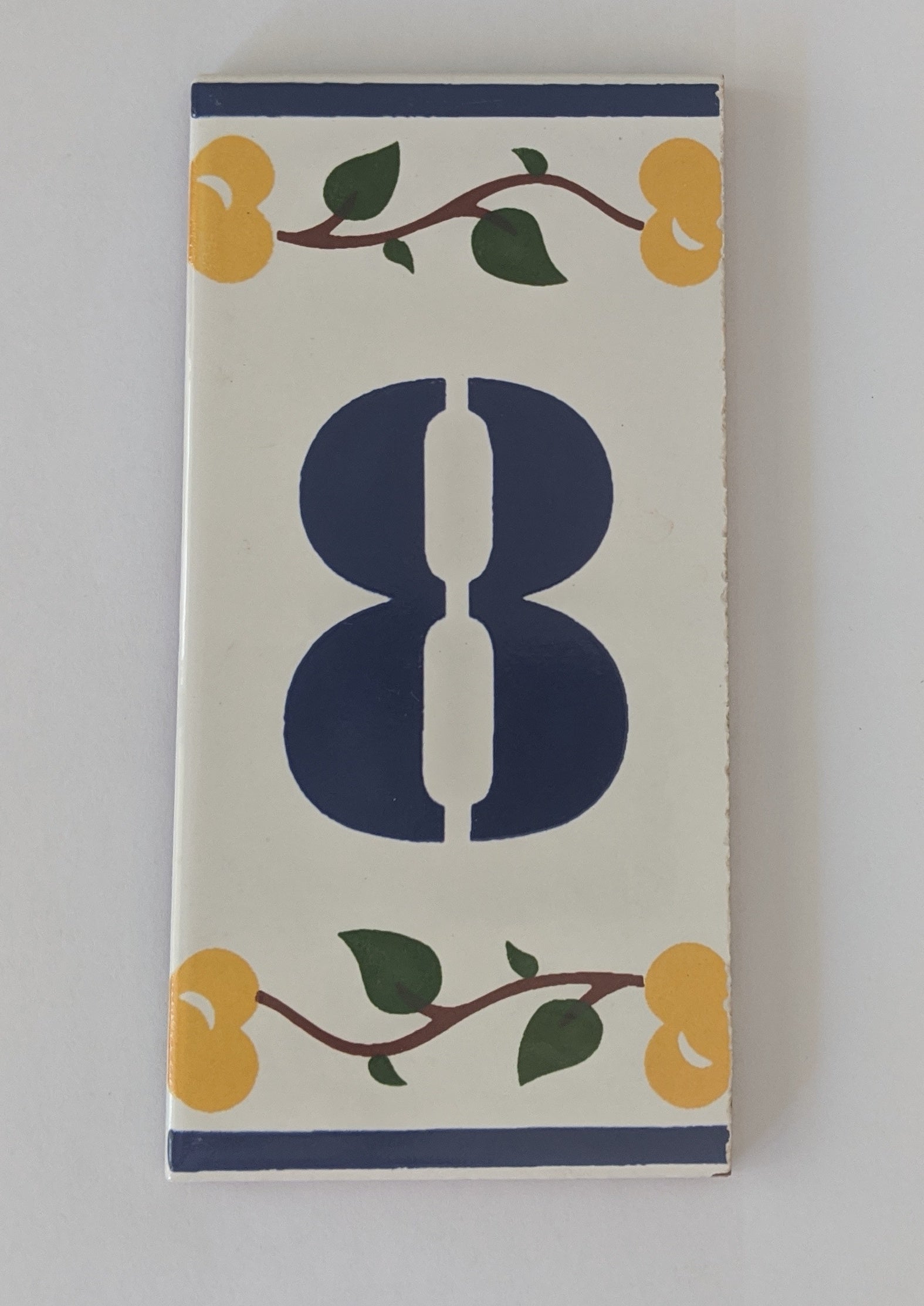 The Iberica Ceramic Number Tiles "Luso" feature a large blue 8 centered on a white background, adorned with yellow flowers and green leaves along the edges—ideal for decorative number tiles or ceramic number signs.