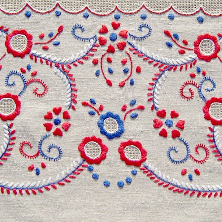 The Terra Lusa "Viana do Castelo" Embroidery Glasses Case features a colorful hand-embroidered floral pattern in red, blue, and white on beige fabric, with stylized flowers and leaves inspired by traditional Portuguese designs.