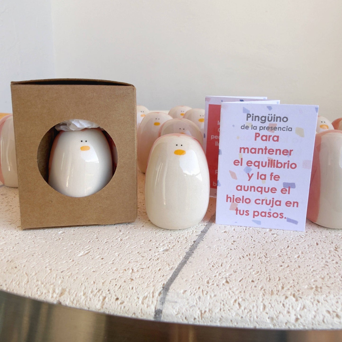 Picuru ceramicas' Penguin Amulet of Presence—a handmade ceramic symbol of balance and resilience—appears in a brown box with a circular window, alongside a Spanish card explaining its meaning.