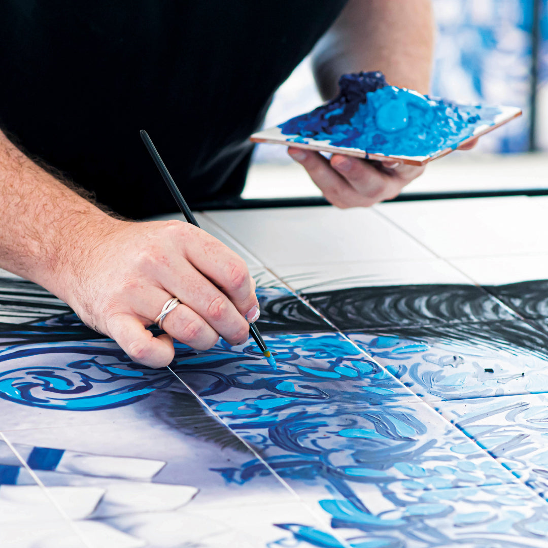 Person painting a blue and white ceramic tile with a brush