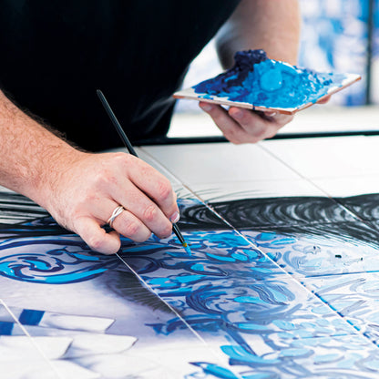 Person painting a blue and white ceramic tile with a brush