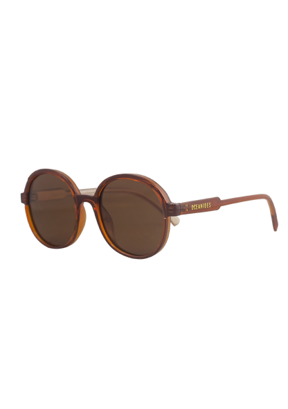 Brisa Crystal Brown Beige Sunglasses by Oceanides feature oversized round frames with dark lenses, a tortoiseshell look, and gold Oceanides branding on the temples—ideal for bold 80s-inspired style against a plain white backdrop.