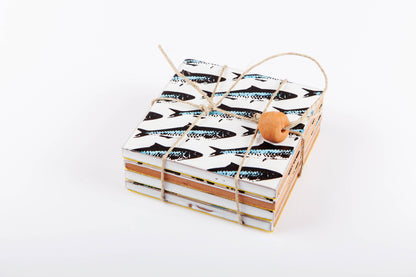 Sardines Coasters by Bussoga: a stack of handmade ceramic coasters featuring a black sardines pattern, tied with twine and a wooden bead, displayed on a white background.