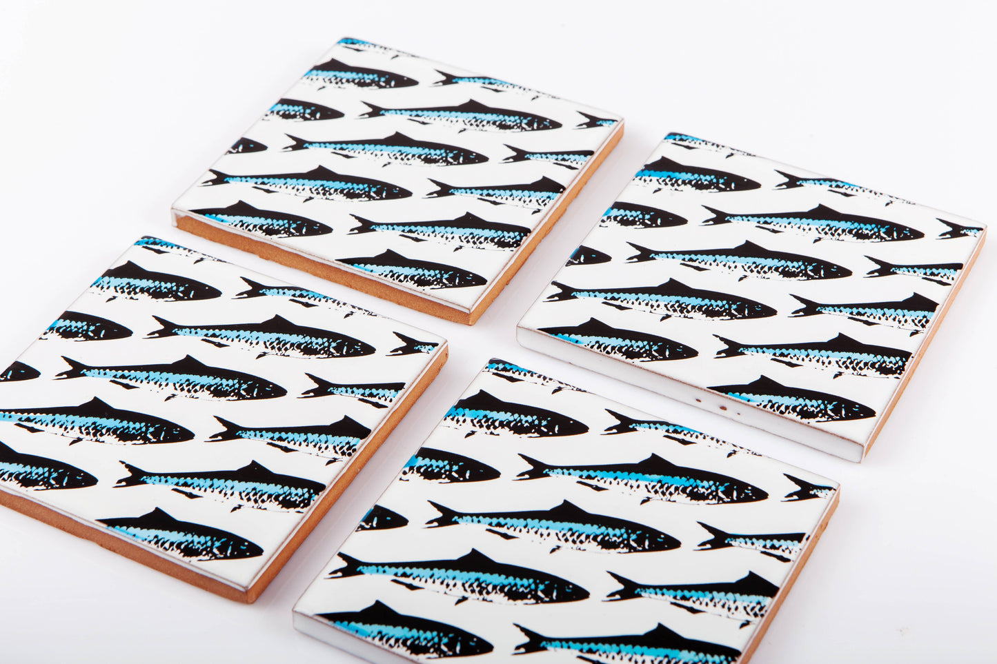 Four handmade Bussoga Sardines Coasters, featuring a repeating black and blue fish pattern, are displayed on a white surface.