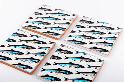 Four handmade Bussoga Sardines Coasters, featuring a repeating black and blue fish pattern, are displayed on a white surface.