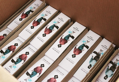 A cardboard box holds several rows of O Melhor do Ribatejo Salt Flower from Portugal, each package illustrated with a person in a hat, red shirt, and blue skirt. The boxes are arranged neatly inside.