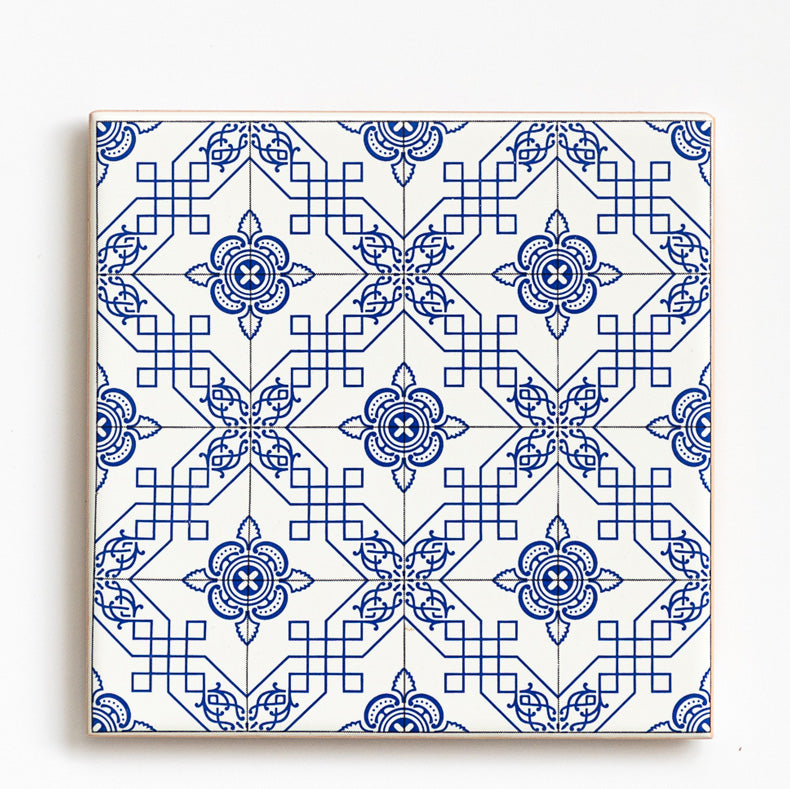 The Ceramic drinks coaster 11cm - Azulejo 24 by ObjectoAnonimo features a blue and white geometric pattern with floral motifs and diamond shapes, echoing traditional Portuguese tile design. Ideal for use as a decorative azulejo coaster.