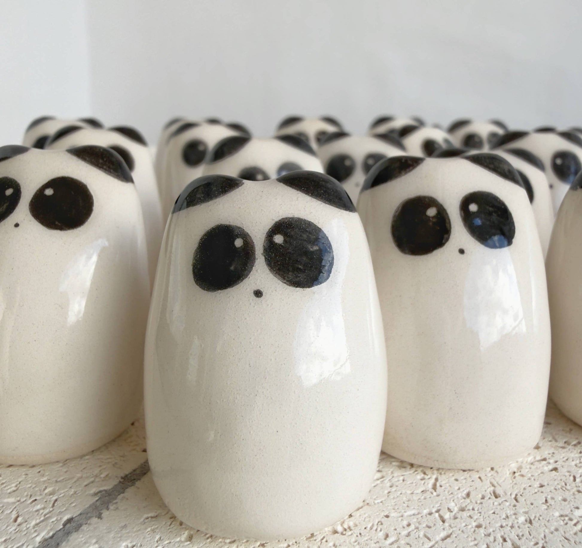 A collection of Picuru ceramicas’ Panda Amulet of Inner Peace – Handmade Lucky Charm Gifts, featuring smooth white ceramic figures with black eyes and spots, is arranged closely on a textured white surface.