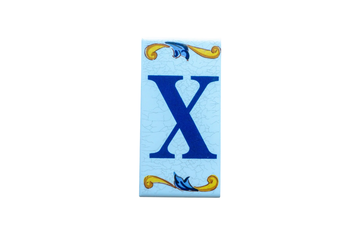 Lisa Croquets Letters – Ceramic House Letter Tiles rectangular tile featuring a blue letter X on a light blue background, accented by decorative yellow and blue scrolls at the top and bottom.