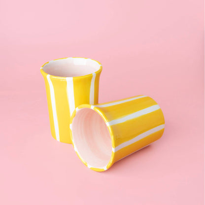 Two Valentina Handmade Spanish Ceramic Mug – Pink & Yellow Stripes mugs, one standing upright and one lying on its side, featuring yellow and white vertical stripes and pink interiors.